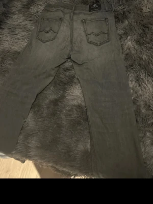 Grå jeans från Replay - Säljer ett par grå jeans från Replay med raka ben och klassiska bakfickor med snygga sömdetaljer. Jeansen har bälteshällor och är tillverkade i ett mjukt denimtyg som känns bekvämt hela dagen.