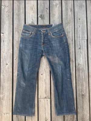  Nudie Jeans bootcut ola  - Säljer ett par klassiska blå jeans från Nudie Jeans med rak passform och fem fickor. Jeansen har snygga slitningar och kontrastsömmar som ger en avslappnad look. Perfekta till en casual outfit och tillverkade i slitstarkt denimtyg.