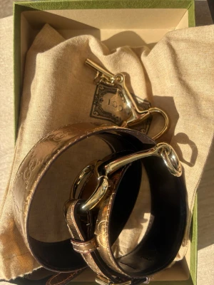 Guccissima embossed leather belt bälte med metallspänne - Snyggt bälte i guldigt skinn med dekorativa detaljer och ett stort, silvrigt metallspänne som påminner om ett bett. Perfekt accessoar för att lyfta din outfit med en unik touch.  Det finns en liten skada på insidan av bältet, men utsidan är hel. 