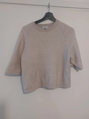 Beige stickad tröja & Other Stories - Säljer en beige stickad tröja från & Other Stories med rund halsringning och halvlånga ärmar. Tröjan har en mjuk och lite boxig passform, perfekt för lager på lager. Materialet känns mysigt och passar till många olika stilar.Den har krymt lite i tvätten men har fortfarande en fin passform.Alpacka