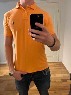 Orange Ralph Lauren pike - Säljer denna sjukt snygga piké från Ralph Lauren⭐️ Färgen är orange och storleken är M✅ Den har inga defekter och skicket är utomordentligt🙌🤝 Sjukt najs passform☀️🙌 Tveka inte på att höra av er dig vid minsta fråga eller fundering😊