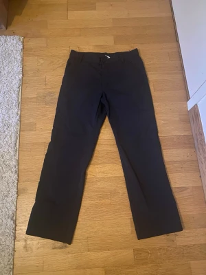 Svarta chinos från Nike - Snygga svarta chinos från Nike med rak passform och klassisk design. Byxorna har diskreta fickor och ett litet Nike-märke på baksidan. Perfekta för dig som gillar en stilren och enkel look.