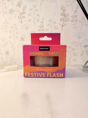 Body Sence Shimmer Balm Festive Flash - Body kropps Shimmer Balm från Sence i färgen Festive Flash. Kommer i en rund burk och är för både ansikte och kropp. Förpackningen är färgglad i rosa, orange och lila toner. Ger ett skimrande glow och är enkel att applicera för en extra glittrig look.