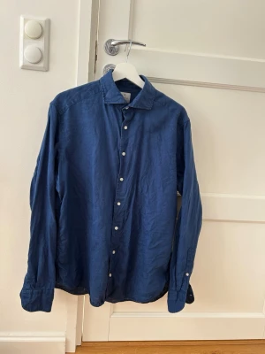 Blå linneskjorta från La Chemise - Snygg blå skjorta i linne med klassisk krage och vita knappar. Skjortan är classic fit och i st 40 vilket är M/L. 100% linne köpt på La Chemise Norrmalm för 900kr, hör  gärna av er vid frågor!
