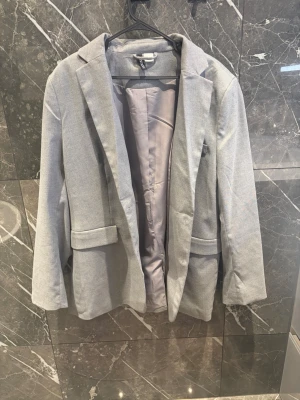 Grå kavaj från H&M  - Stilren och snygg kavaj från H&M i storlek M.   Endast använd en gång och är i mycket bra skick. Fin passform och lätt att matcha med både jeans, kostymbyxor och kjol. Passar perfekt både till vardags, jobbet och finare tillfällen.  Kan självklart skicka fler bilder eller mått vid intresse! 🤍