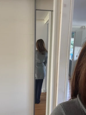 Ljusgrå lång kofta med knytband - Ljusgrå lång kofta i mjukt material med stora svarta knappar framtill och ett matchande knytband i midjan. Koftan har ribbad krage, långa ärmar och en avslappnad passform som ger en chill vibe. Passar även S då den har midjeband