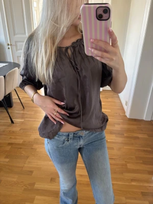 Brun glansig blus med knytning - Snygg brun glansig blus med avslappnad passform och knytning vid halsen. Blusen har trekvartsärm och ett lätt tyg. Skriv för mer info😊