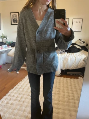 Grå oversized kofta med fickor - Mysig grå kofta med stora knappar och två framfickor. Oversized passform med breda ärmar och ribbade muddar vid ärmslut och nederkant. Perfekt att slänga på sig över en t-shirt för en avslappnad look.