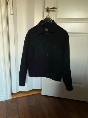 Marinblå overshirt från Zara - Marinblå overshirt med klassisk krage och knäppning framtill. Två bröstfickor med lock och knappar ger en clean look. Långa ärmar med knapp vid ärmslut. Perfekt för lager på lager och enkel att styla.