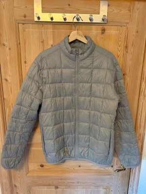 Grå pufferjacka från Jack & Jones - Snygg grå pufferjacka från Jack & Jones med quiltat mönster och dragkedja framtill. Jackan har hög krage och två sidofickor. Perfekt för kalla vinterdagar och enkel att matcha med olika outfits.