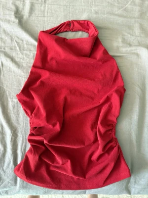 Röd halterneck topp - Snygg röd halterneck topp med knäppning i nacken. Toppen är ärmlös och har en tight passform med rynkade sidor för en cool look. Perfekt för dig som vill sticka ut med en färgstark och trendig topp. Använt en gång.