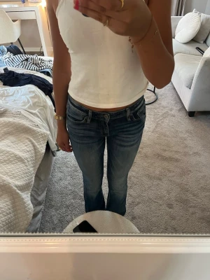 Blå bootcut jeans med slitningar - Säljer ett par blå bootcut jeans med snygga slitningar och klassisk femficksdesign. Jeansen har låg midja och är i ett mjukt denimtyg som sitter skönt. Perfekta för en avslappnad och trendig look.