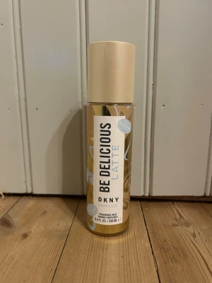 DKNY Be Delicious Latte Vanilla mist - Fräsch och söt doftmist från DKNY i serien Be Delicious Latte Vanilla. Flaskan är cylinderformad i plast med beige och guldiga detaljer samt en beige kork. Innehåller 250 ml och har en smidig sprayfunktion. Perfekt för dig som gillar vaniljdoft.