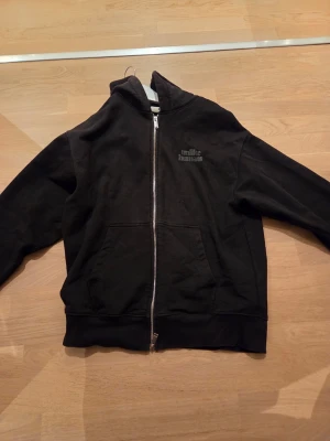 Svart hoodie med dragkedja - Säljer en svart hoodie med dragkedja och fickor framtill. Trycket 'mike humans' syns på bröstet. Hoodien har en klassisk huva och ribbade muddar vid ärmslut och nederkant. Perfekt för en avslappnad och stilren look.