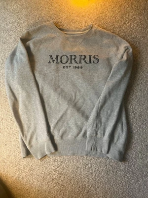 Grå sweatshirt från Morris - Nypris ca 1200kr Snygg grå sweatshirt från Morris med svart tryck 'MORRIS EST 1968' på bröstet. Klassisk rund halsringning och ribbade muddar vid ärmslut och nederkant. Perfekt för en avslappnad och stilren look.