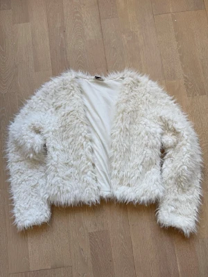 Vit fluffig teddyjacka - Säljer en supermjuk och fluffig vit teddyjacka med lång ärm och öppen front. Jackan har en kortare, boxig passform. .