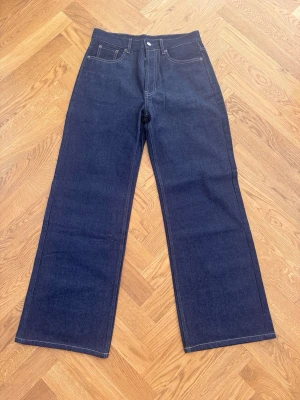 Acne jeans - Säljer ett par mörkblå jeans med raka ben och hög midja. Klassisk femficksmodell med kontrastsömmar och knappgylf. Jeansen har en clean look utan slitningar och är tillverkade i kraftig denim. Perfekta för dig som gillar en tidlös och enkel stil.