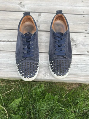 Mörkblå louboutins med bitar - Säljer ett par snygga Mörblå med nitar skorna har tecken på användning vissa nitar har tappat lite färg och insidan av skon är också lite sliten inget som syns med skon på eller som känns när man går, mockan är fortfarande i bra skick och sulan går att tvättas upp, för fler frågor är det bara att skriva 🙌 box extra nit och extra snören ingår i köp!