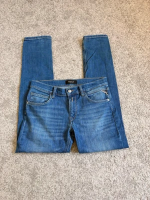 Blå jeans från Replay - Säljer ett par klassiska blå jeans från Replay med fem fickor och raka ben. Jeansen har snygga slitningar framtill och en patch med Replay-logga bak i midjan. Tillverkade i mjukt denimtyg som sitter skönt och har en tidlös look. Storlek 158, hör av er vid funderingar😀