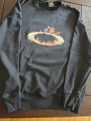 Oakley svart sweatshirt - Cool svart sweatshirt från Oakley med tryxk på framsidan. Endast använd fåtal gånger, säljer p.g.a den satt lite för baggy. Den är egentligen S men sitter baggy så skulle nog kunna passa M. Annars är materialet bra