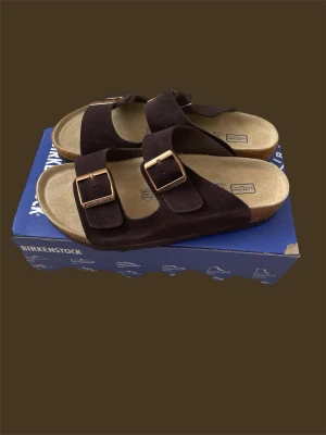 Birkenstock Arizona Soft Footbed, Strl 41, Helt nya - Säljer ett par helt nya Birkenstock Arizona Soft Footbed i mörkbrun mocka med klassiska spännen. En av Birkenstocks mest populära modeller, känd för sin komfort, höga kvalitet och tidlösa design.  Skorna är helt oanvända och kommer i originalkartong. Perfekta inför sommaren eller som bekväma vardagssandaler.  Storlek: 41  Skick: • Helt nya • Oanvända • Originalkartong ingår  Nypris: cirka 1 600 till 1 900 kr.