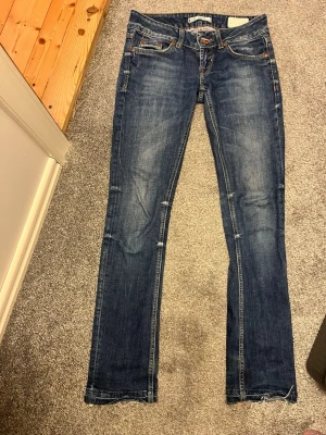 Blå raka jeans från LTB - Snygga blå jeans från LTB med raka ben och slitna detaljer. Klassisk femficksmodell med orangea sömmar och knappgylf. Jeansen har en tvättad look och är tillverkade i bomull med lite stretch för skön passform.