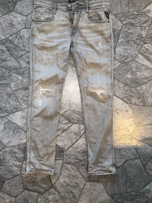 Grå replay jeans med slitningar - Säljer ett par ljusgrå jeans från Replay med skinny fit och slitningar på låren och knäna. Jeansen har fem fickor, dragkedjegylf och coola detaljer vid fickorna. Perfekta för dig som gillar en avslappnad och trendig stil. W30/31 och L30. Pris kan diskuteras:)