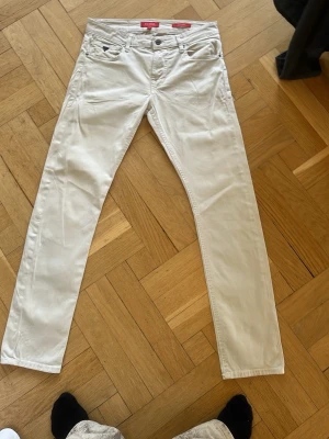 Vita slim fit jeans från Guess - Snygga vita slim fit jeans från Guess med klassisk femficksdesign och diskret logga på myntfickan. Jeansen har normal midja och raka ben. Perfekta för dig som vill ha en clean och fräsch look.