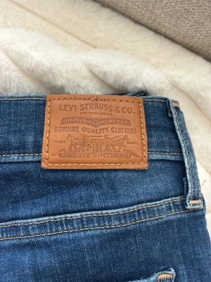 Blå Levi's jeans med klassisk passform - Säljer ett par blå jeans från Levi's med klassisk femficksmodell och tydliga kontrastsömmar. Jeansen har en brun läderpatch bak i midjan och den ikoniska röda Levi's-taggen på bakfickan. Skinny modell. 