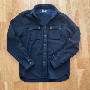 Nudie Jeans Wool Overshirt  - Svart Nudie Jeans overshirt i storlek M, tillverkad i Portugal. Rejäl ullblandning med 60% ull. Bra begagnat skick, endast lätt nopprig på vissa ställen på grund av normal användning. Perfekt som overshirt eller lättare jacka.