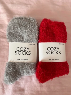 Mysiga fluffiga cozy socks - Två par supermjuka och fluffiga cozy socks i grått och rött. Perfekta för kalla dagar när du vill ha det extra varmt om fötterna. One size och riktigt gosigt material som känns skönt mot huden.