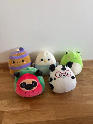 Fem mjuka Squishmallows gosedjur.  - Säljer ett gäng Squishmallows i olika former och färger: en grön groda, en vit och blå fågel, en brun bakelse med lila, en rosa och grön vattenmelonhund samt en vit och svart dalmatiner med röda glasögon. Perfekta som kramdjur eller dekoration! Endast lagt i en låda sedan dom köptes. I vanliga fall kostar ett gosedjur ca 150kr.