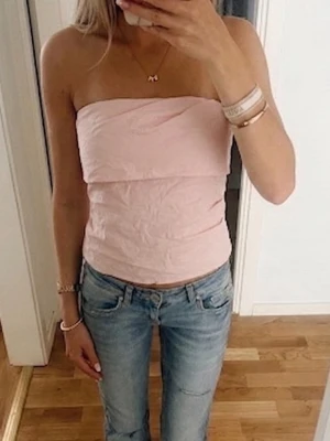 Ljusrosa bandeau tubtopp - Säljer en ljusrosa bandeau tubtopp som är axelbandslös och har en enkel, stilren design. Toppen är croppad och passar perfekt till jeans eller kjol. Materialet känns mjukt och lätt, perfekt för varma dagar. Lappen på insidan av tröjan som visar märket är halvt sönder men det är inget som syns när man har på sig den 🩷