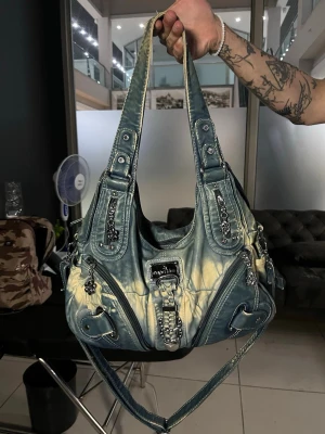 Y2k handväska med kedjedetaljer - Cool handväska i blått tie-dye-mönster med silvriga kedjor och spännen. Väskan har flera dragkedjor, dekorativa remmar och en justerbar axelrem. Perfekt för dig som gillar en edgy och unik stil.  Den är helt ny!