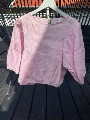 Ljusrosa blus från Carin Wester - Säljer en ljusrosa blus från Carin Wester med trekvartsärm och rund halsringning. Blusen har en lätt krinklad struktur och knäppning bak i nacken. Perfekt för en trendig och avslappnad look.