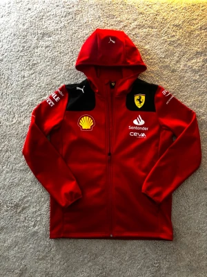 Ferrari F1 x Puma softshell jacket-Team issue size M - Puma scuderia ferrari f1 fleece. Nästan helt oanvänd och köpt ny i ferrari museet i Italien. Full zip med huva utan några som helst skador. Sponsorer: Shell, Santander, CEVA Logistics, pirelli, Puma. Samt en ferrari sköld vid bröstet