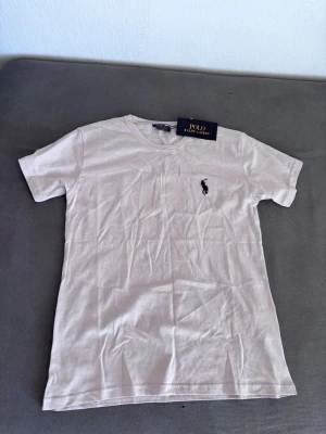 Vit t-shirt från Polo Ralph Lauren - Klassisk vit t-shirt från Polo Ralph Lauren med korta ärmar och rund hals. T-shirten har den ikoniska loggan broderad i svart på bröstet. Tillverkad i mjuk bomull för en skön känsla och enkel stil.