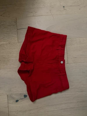 Röda shorts med fickor - Snygga röda shorts med klassisk femficksdesign och knappstängning fram. Shortsen har bälteshällor och är perfekta för varma dagar. Passformen är normal och materialet känns som bomull, vilket gör dem bekväma och lätta att bära.