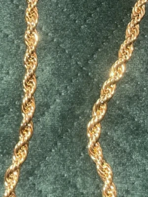 Guldfärgat tvinnat halsband - Snyggt halsband i guldfärg med tvinnad kedja som ger en cool och trendig look. Halsbandet har en glänsande finish och passar perfekt för dig som gillar stilrena accessoarer. Materialet ser ut att vara metall med en guldfärgad yta.