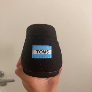 Svarta loafers från Toms  - Säljer ett par svarta TOMS från The Venice Collection. Skorna är i nyskick då skorna aldrig använts och har en färgglad randig insida. Perfekta för en avslappnad stil och passar bra till både vardag och fest. 