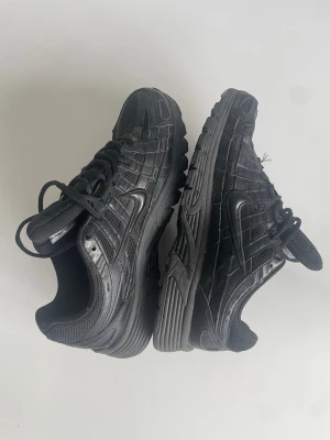 Svarta sneakers med mesh och skinn - Snygga helsvarta sneakers med en mix av mesh och skinnpaneler. Skorna har en sportig siluett, grov sula och klassisk snörning. Perfekta för dig som gillar en clean och stilren look till vardags. Diskret logga på sidan och vadderad häl för extra komfort.