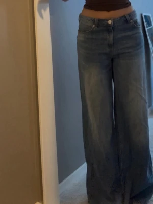 Blåa wide leg jeans med hög midja - Säljer ett par blåa straight jeans. Jeansen har klassiska fickor fram och bak, stängs med knapp och dragkedja. Perfekta för en avslappnad och trendig look. 