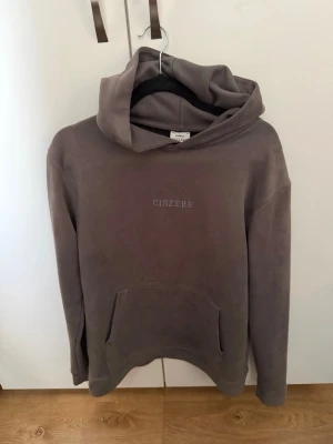Brun hoodie från Ciszere med huva - Snygg brun hoodie från Ciszere med broderad logga på bröstet. Hoodien har en stor känguruficka framtill och en rejäl huva. Tillverkad i mjukt material som känns skönt mot huden. Perfekt för en avslappnad och stilren look.