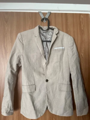 Beige kavaj, storlek 158 - Superfin beige med linnekänsla kavaj i storlek 158 från H&M. Sparsamt använd utan defekter vad jag kan se. Kavajen är en blandning mellan bomull (78%) och linne (22%)