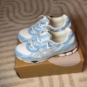  Nya oandvända Blåvita sneakers från Asics - Snygga sneakers från Asics i ljusblått och vitt med klassiska ränder på sidan. Ovandelen är i mesh och mockaliknande material, sulan är vit med grå detaljer. Perfekta för dig som gillar sportig och trendig stil.