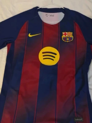 FC Barcelona matchtröja Lamine Yamal - Säljer en officiell FC Barcelona matchtröja från Nike med Lamine Yamal och nummer 10 på ryggen. Tröjan har klassiska blå och röda ränder, gula detaljer och klubbmärke på bröstet. Tillverkad i ett lätt och funktionellt material, perfekt för fotbollsträning eller match. Passar för både s och m