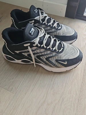 Nike Air Max TW svart/vit sneaker - Nike Air Max TW sneakers i svart och vitt med mesh- och syntetmaterial. Skorna har tydliga Air Max-detaljer, vita snören och en chunky sula med synliga luftbubblor. Snyggt mönster på sidan och klassisk Nike Swoosh på tån.
