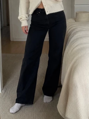 Svarta raka jeans från Levi's - Säljer ett par svarta raka jeans från Levi's med klassisk femficksmodell och hög midja. Jeansen har en snygg vintagekänsla och är tillverkade i kraftig denim med läderpatch bak. Perfekta till en avslappnad och trendig look. Storlek 30