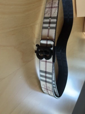 Burberry bälte  - Du får med allt som syns på bild 3 för ett riktigt schysst pris!! Snyggt bälte med klassiskt rutigt mönster i svart, vitt och beige. Bältet är gjort i skinn och har flera hål för justering. Perfekt accessoar för att lyfta din outfit. 