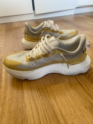 Vita och gula sneakers från Under Armour - Snygga sneakers från Under Armour i vitt och gult med svarta detaljer. Ovandelen är i mesh för bra ventilation och sulan är tjock och vit för extra komfort. Skorna har klassisk snörning och en sportig look som sticker ut.